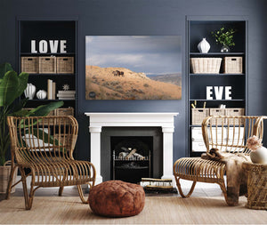 a cozy living room with a fireplace, wicker chairs, and a large framed landscape photograph on the wall.