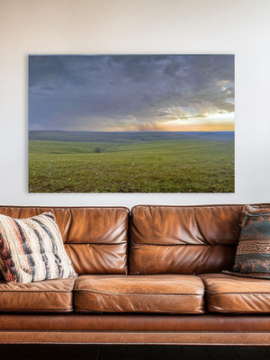 a large landscape painting hanging on a wall above a brown leather couch with patterned pillows.