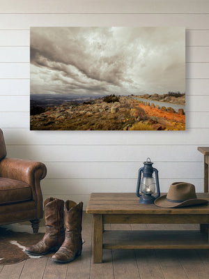 a rustic living room with a large landscape painting hanging on the wall, a wooden coffee table with a lantern and a hat, and a pair of cowboy boots placed on the floor.