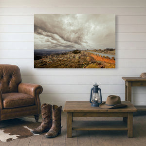 a rustic living room with a large landscape painting hanging on the wall, a wooden coffee table with a lantern and a hat, and a pair of cowboy boots placed on the floor.