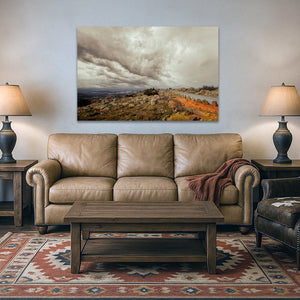 a living room with a large, brown leather couch, a wooden coffee table, and two lamps on either side of the couch. Above the couch, there is a large painting depicting a scenic landscape with mountains and a river.