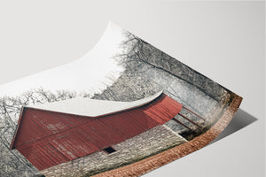 A red barn with a sloping roof stands in a wooded area, surrounded by bare trees.