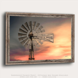A framed print depicting a windmill against a colorful sunset sky.