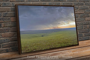 A framed landscape photograph depicting a rolling green field with a dramatic sky in the background, possibly during a sunset or sunrise.