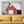A large rectangular wall art print showing a red barn with a white roof, displayed above a mustard yellow sofa in a modern living room setting.