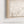 The image is a close-up of a natural maple float-framed canvas frame with a blurred field of tall grass in the background.