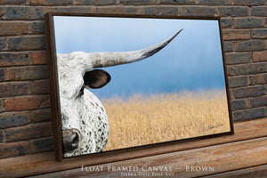 A framed canvas depicting a close-up of a bull's head with a field of tall grass in the background.
