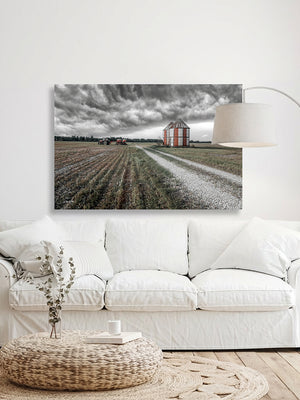 a living room with a white sofa, a coffee table, and a large painting of a farm scene hanging on the wall above the sofa.