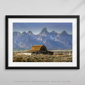 a framed photograph of a barn in front of a mountain range