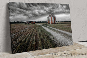 A large, red and white barn stands in a field, with a tractor parked in the distance. The sky is filled with dark clouds, creating a dramatic atmosphere.