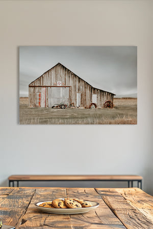 a rustic wooden barn with a large door and a smaller door, set against a cloudy sky. In the foreground, there is a plate of cookies on a wooden table.