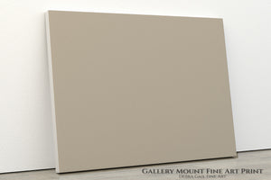 A plain, beige-colored canvas or painting is leaning against a white wall.