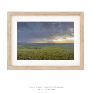 The image is a framed photograph of a grassy field with a dramatic sky in the background, possibly depicting a sunrise or sunset.